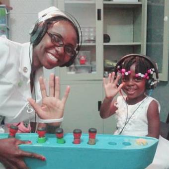 Nurse Precious Nyanga with three-year old child assessing hearing loss through play audiometry